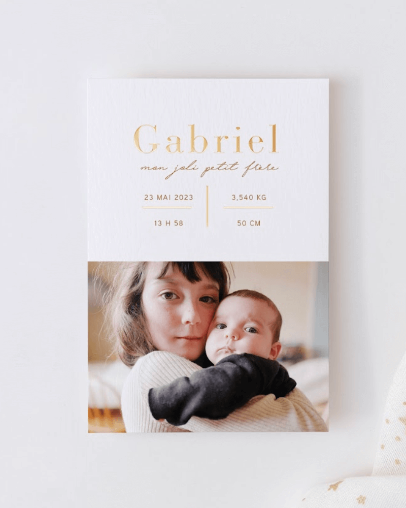 faire-part de naissance avec le prénom Gabriel inscrit en lettres dorées et une photo d’une petite fille et de son petit frère dans ses bras.