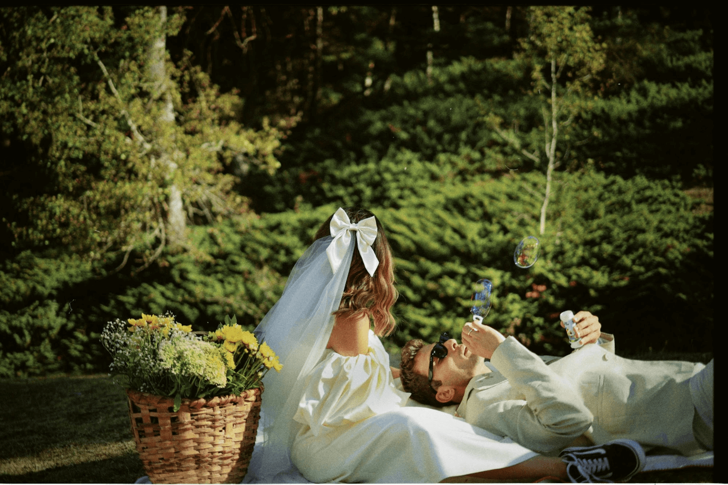 Un couple de jeunes mariés assis dans un parc, entouré de verdure.