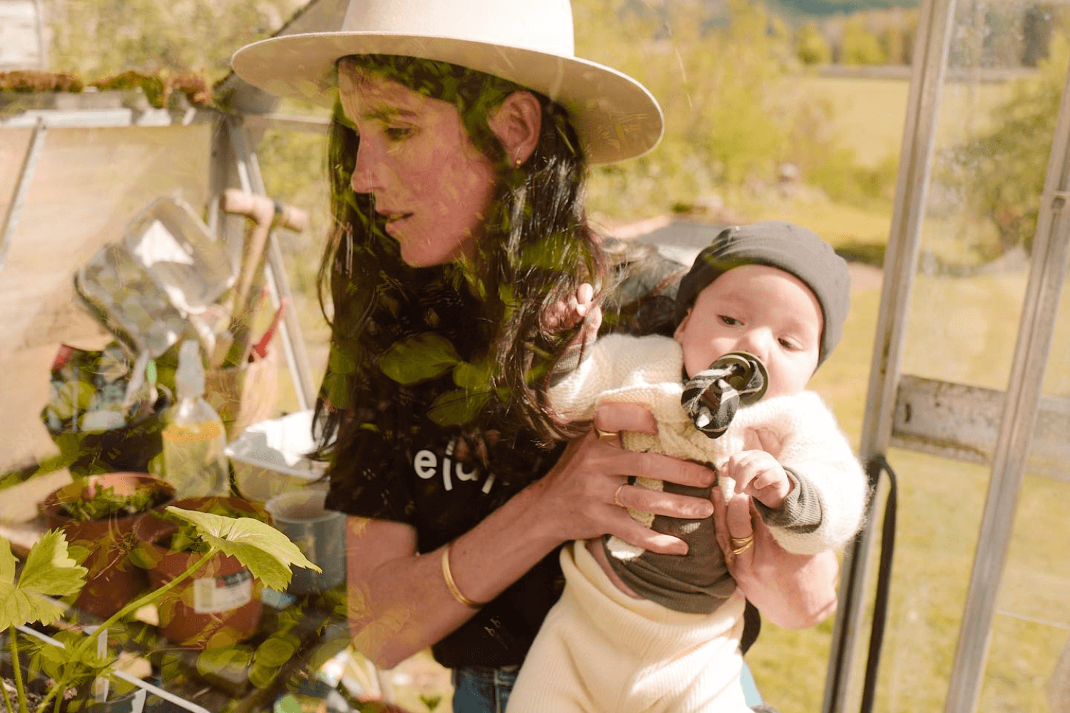une maman dans une serre entourée de plantes, portant dans ses bras son nouveau-né