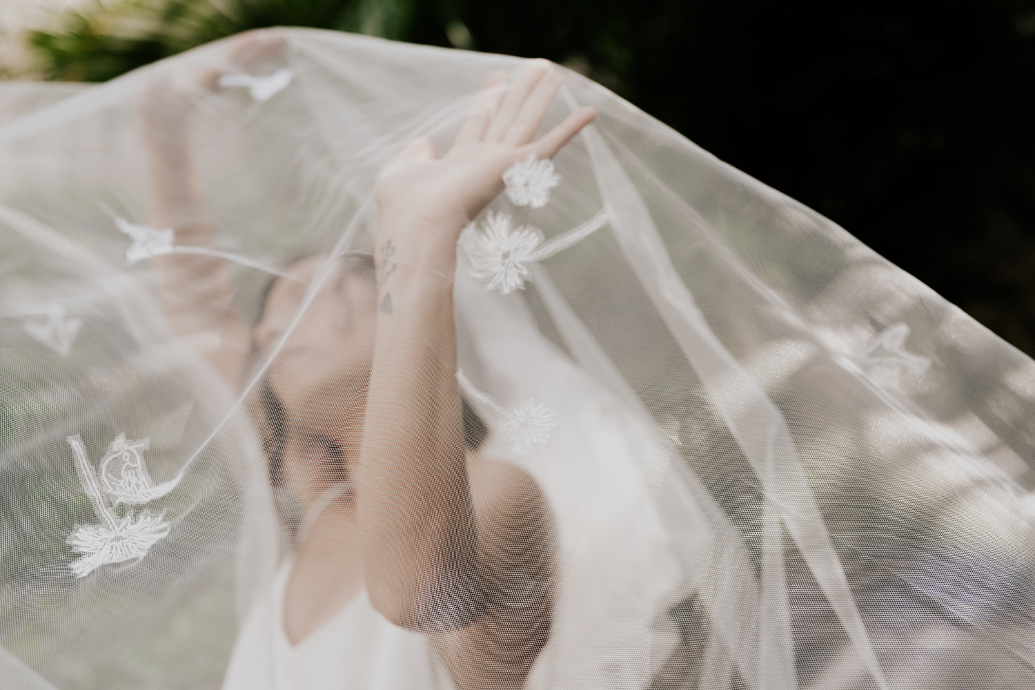 Une jeune mariée tenant son voile de mariée brodé de fleurs, au-dessus de sa tête.