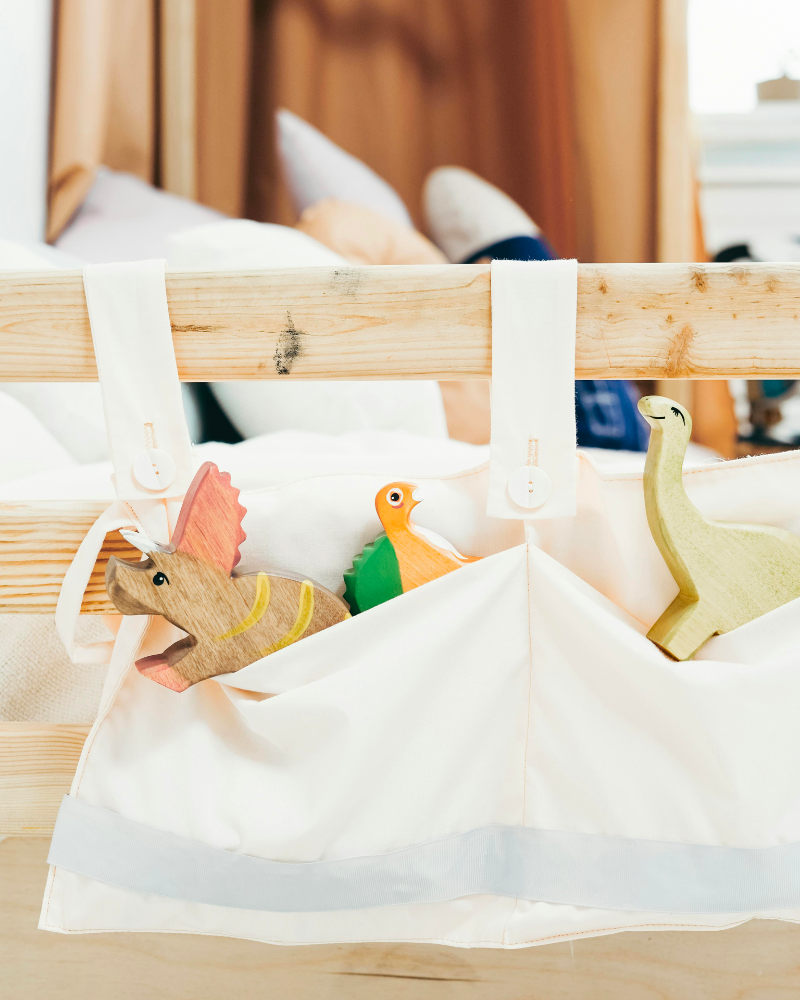 des jouets en bois en forme de dinosaures installés dans une pochette en tissu, accrochée au lit.