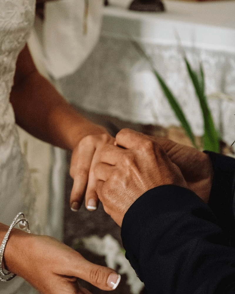 des mains de jeunes mariés, la main de l’homme tenant celle de sa future femme pour lui passer l’alliance.