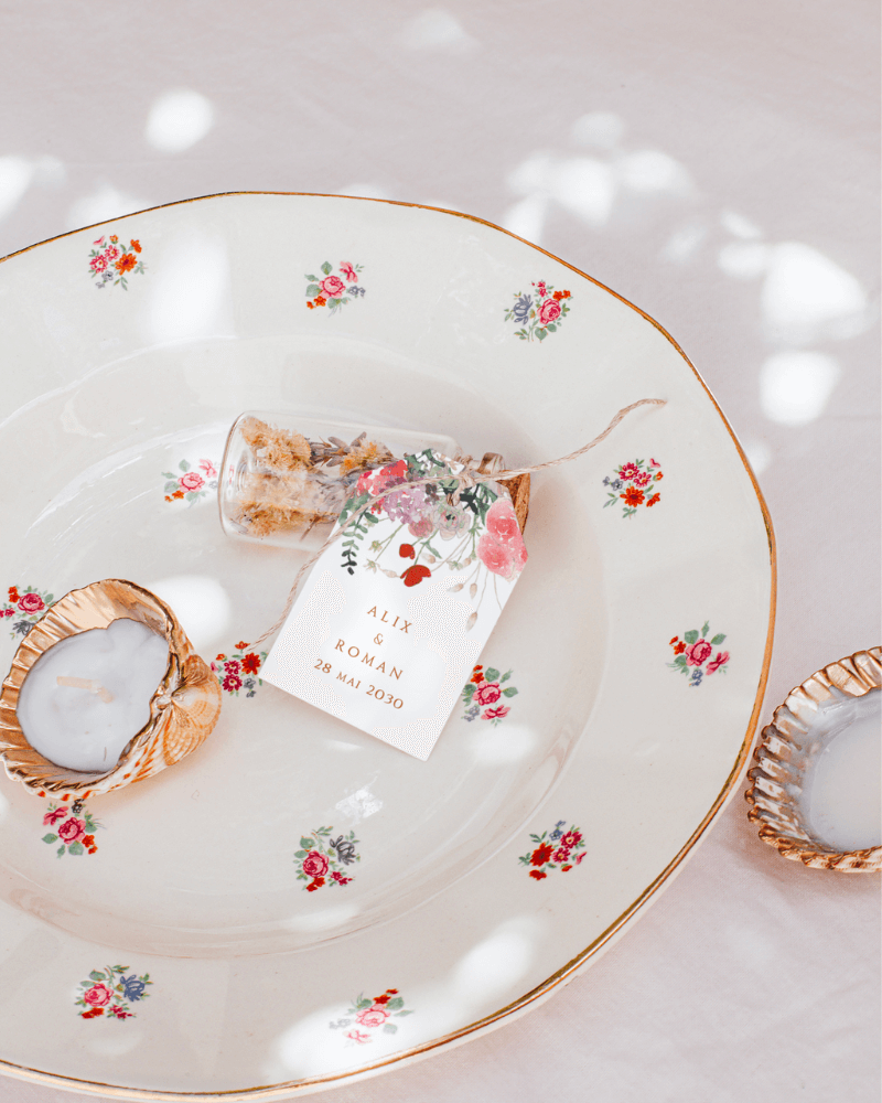 Une étiquette cadeau de mariage avec des illustrations de fleurs en aquarelle, déposée sur une assiette vintage aux motifs fleuris