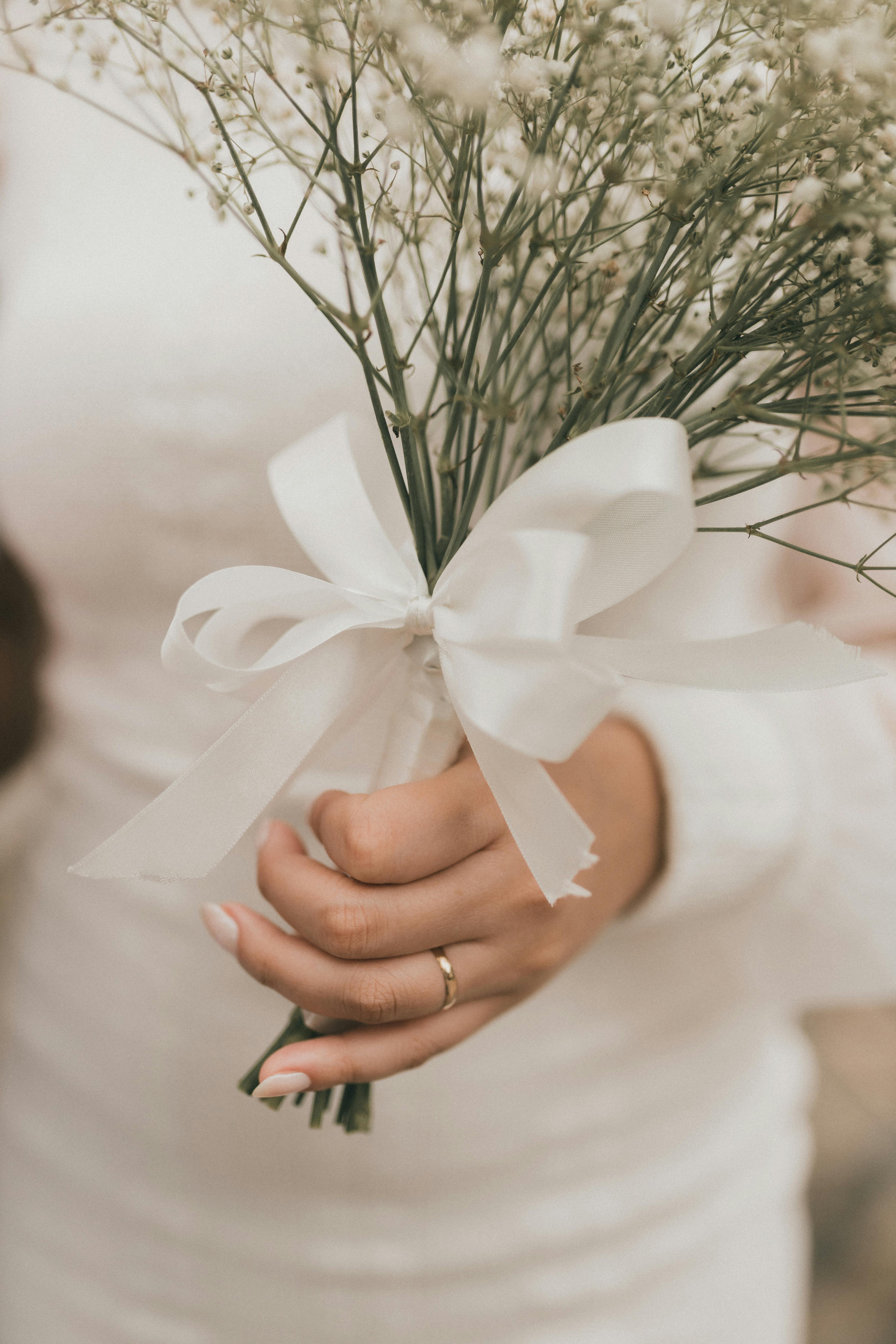 un zoom sur la main d’une mariée, alliance au doigt, tenant dans sa main un bouquet de délicates fleurs de gypsophile.