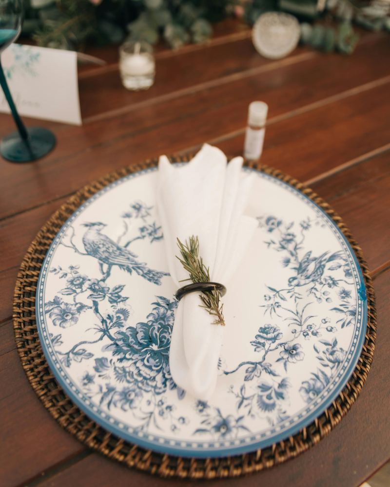 assiette de mariage en porcelaine vintage avec illustrations de couleur bleue d’oiseau et de fleurs, surmontée d’une serviette en tissu.