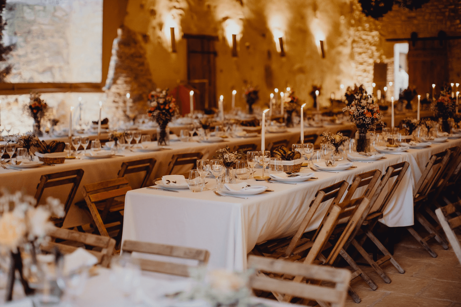 Une table de mariage en bois ornée d’une nappe blanche, entourée de chaises en bois dans un décor vintage.