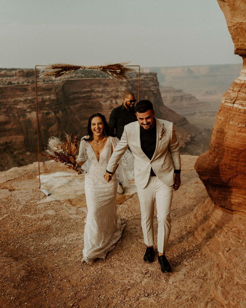 deux mariés main dans la main, souriants, dans un décor semblable au grand Canyon.