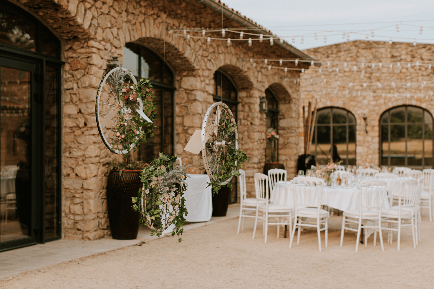 Un lieu de réception de mariage extérieur avec chaises et tables blanches, aux côtés d'une maison de pierres.
