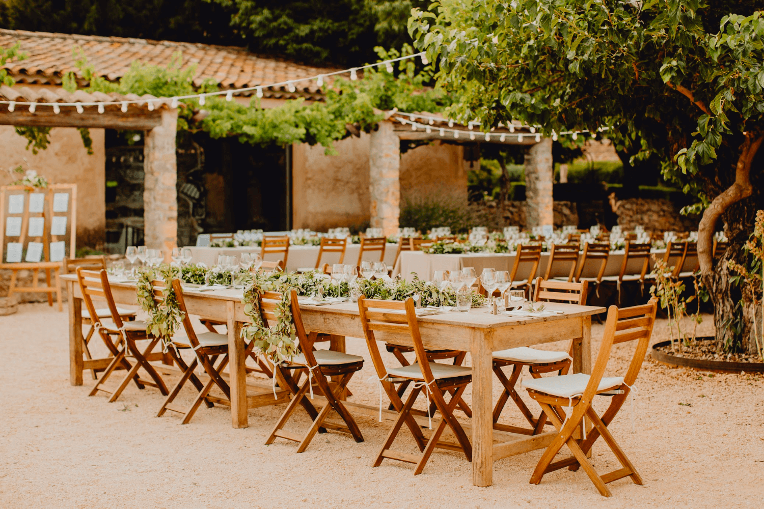 Une table de mariage champêtre en bois en extérieur, décorée d'un chemin de table végétal et entourée de chaises en bois.