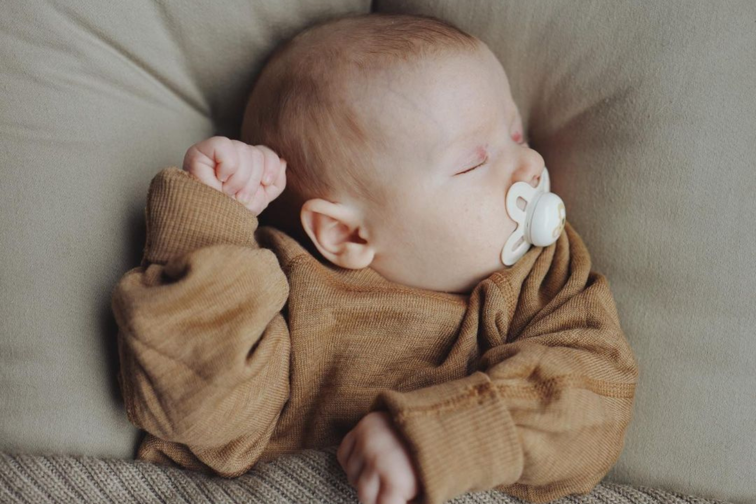 Enfant endormi, portant un petit pull brun.