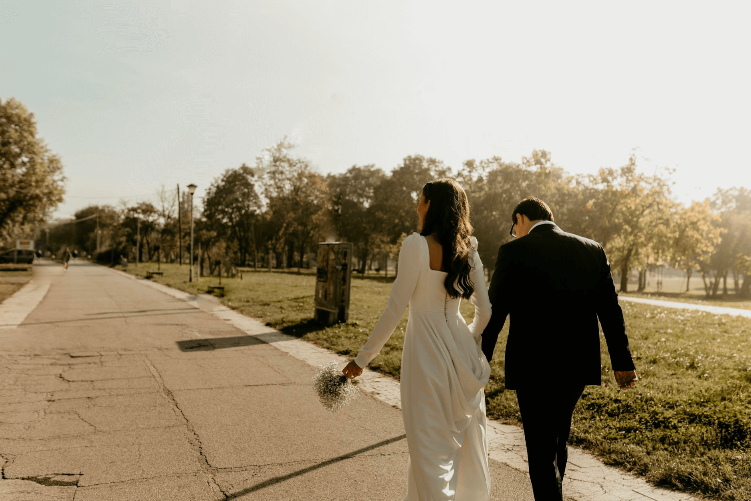 Un couple de jeunes mariés vus de dos, marchant dans un parc.