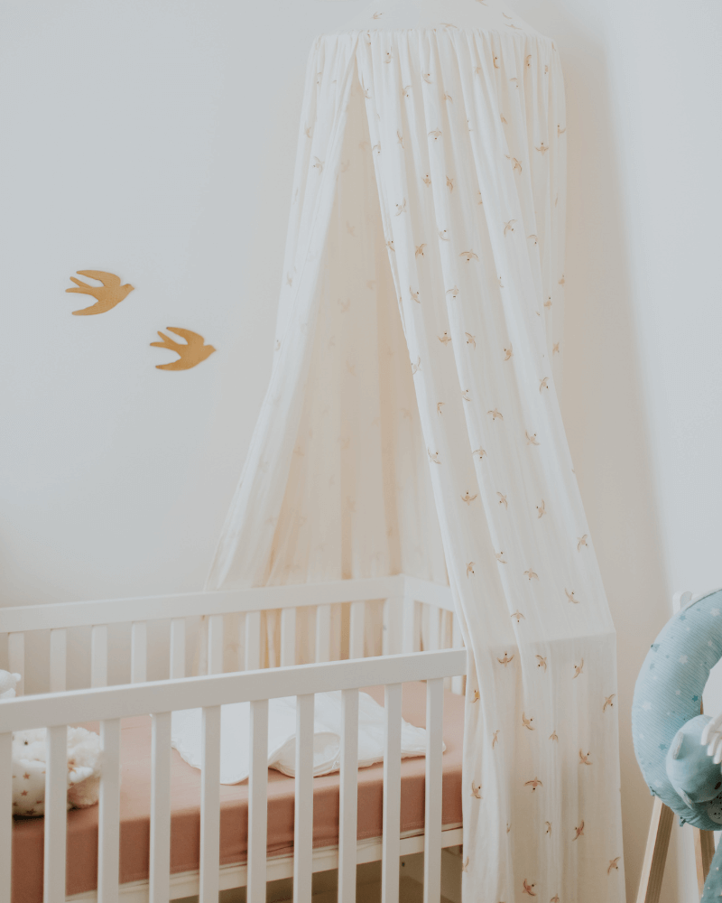 un lit à barreau pour bébé surmonté d’un ciel de lit aux motifs d’oiseaux dorés