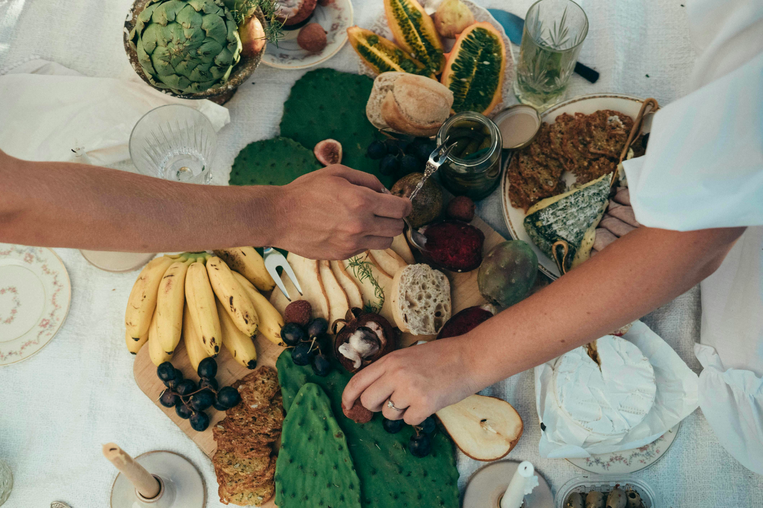 table de brunch mariage vue de haut avec des fromages, des fruits et deux mains se servant