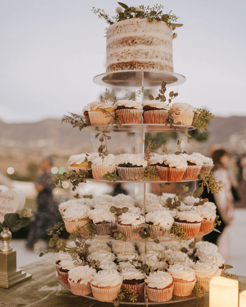 un plateau à plusieurs étages rempli de cupcakes, au sommet se trouve un cake de mariage.