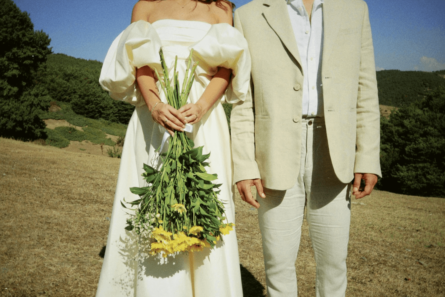 Un couple de jeunes mariés enlacés, un grand bouquet de fleurs et de végétaux entre eux.