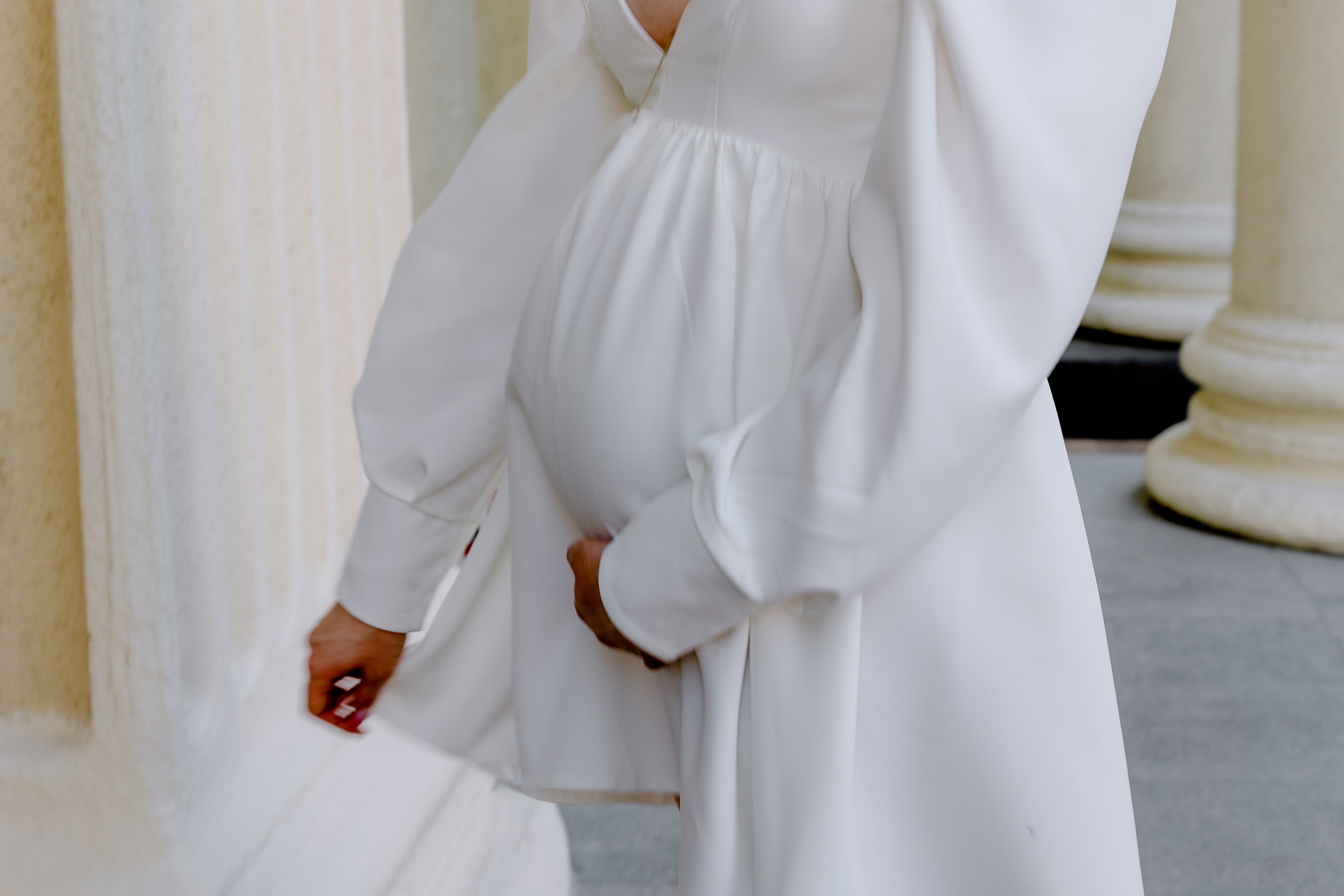 femme enceinte vêtue d’une robe blanche, tenant son ventre arrondi d’une main