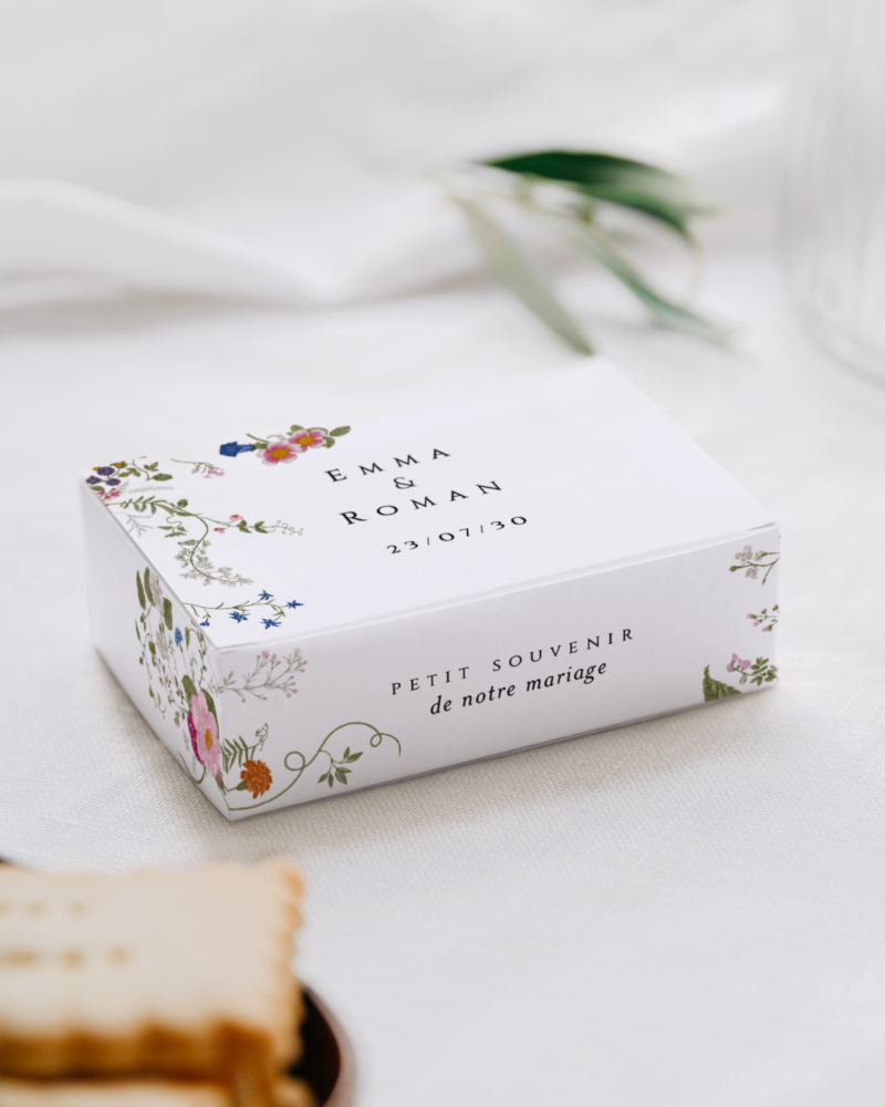 Une boîte à biscuits personnalisée avec les prénoms des mariés et illustrée de fleurs sauvages colorées.