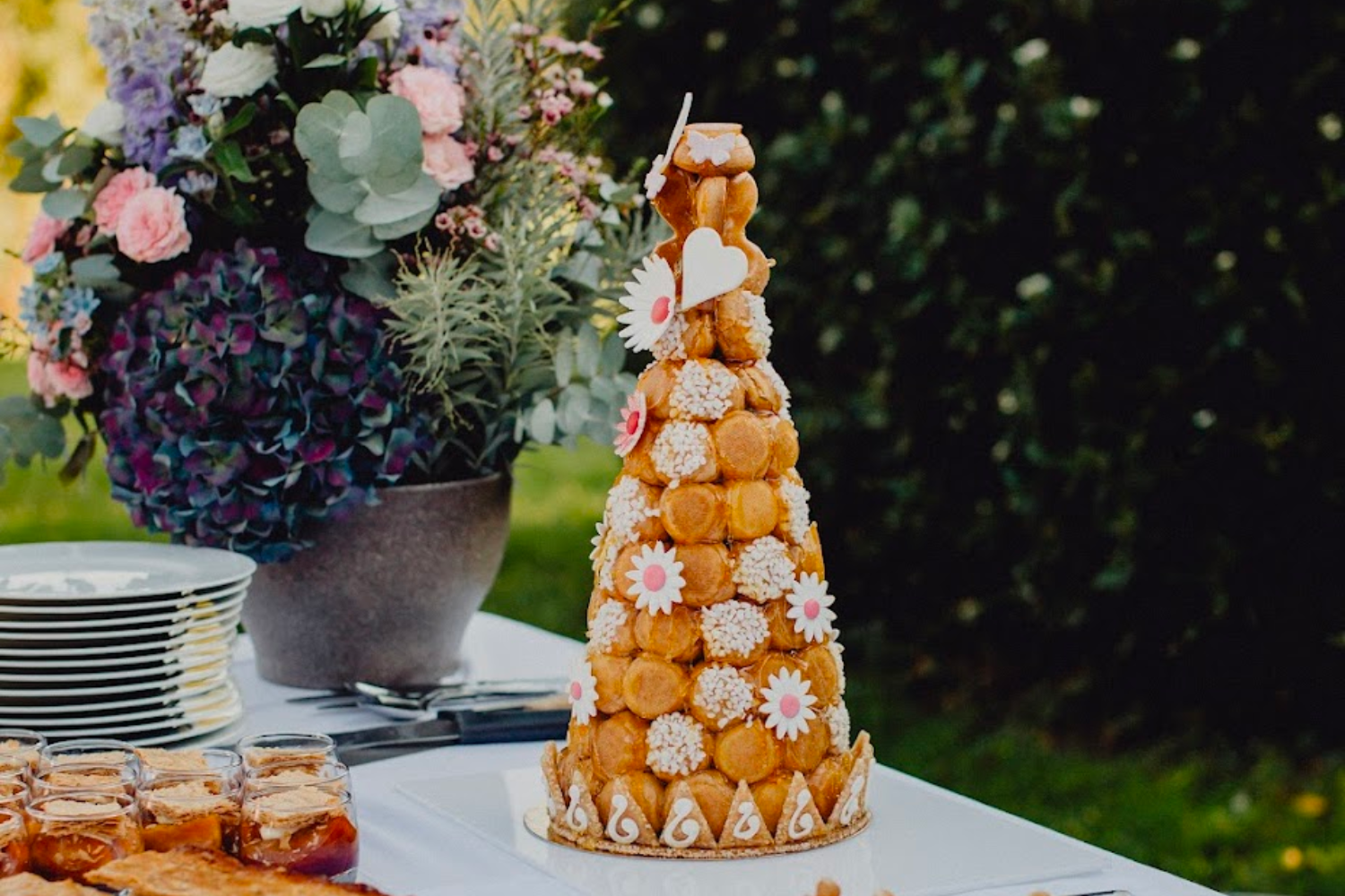 Une pièce montée de mariage croquembouche, décorée de fleurs et de cœurs en sucre blancs.