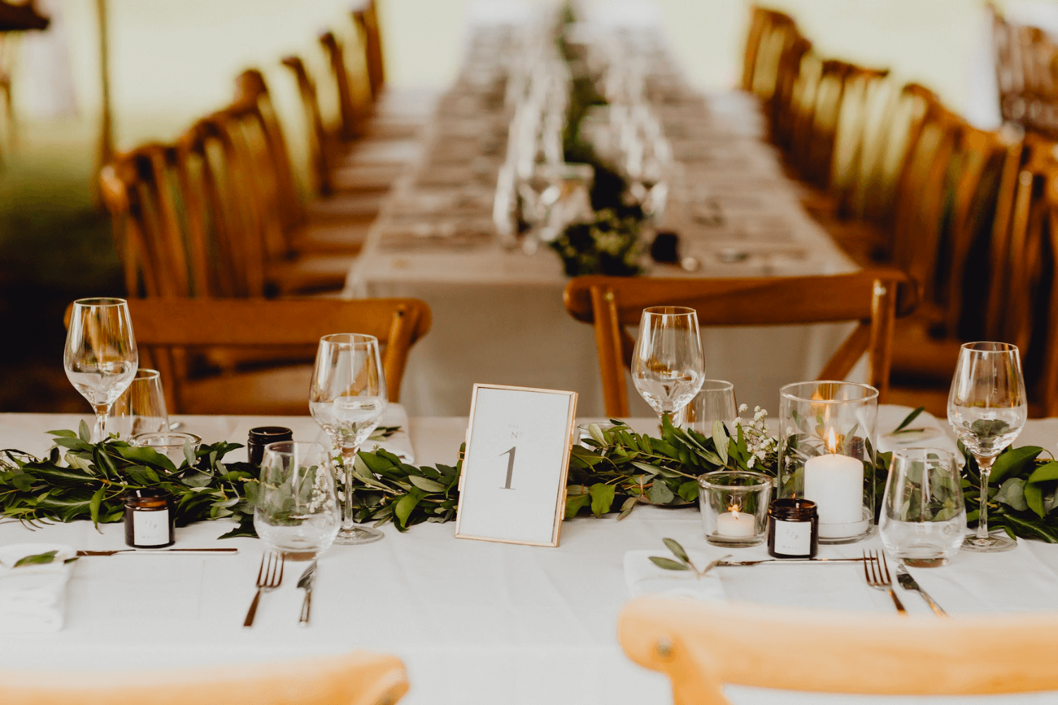 Une table de mariage recouverte d'une nappe blanche et agrémentée d'un chemin de table végétal.