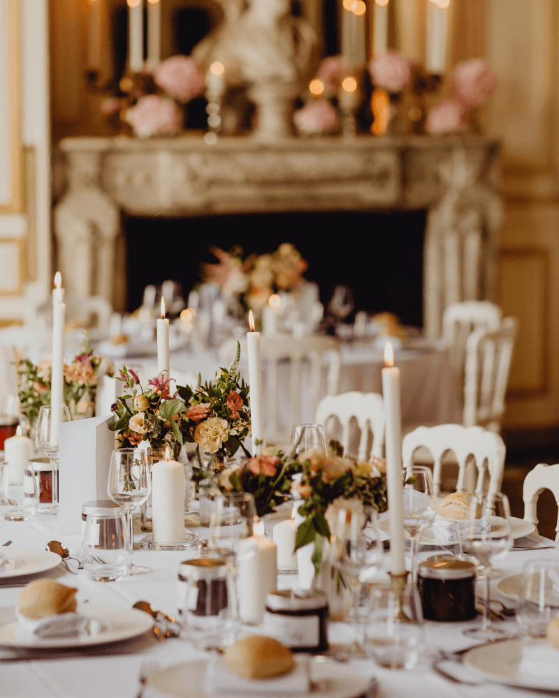 Une table de mariage blanche dressée dans un salon. En arrière plan, on aperçoit une cheminée ancienne.