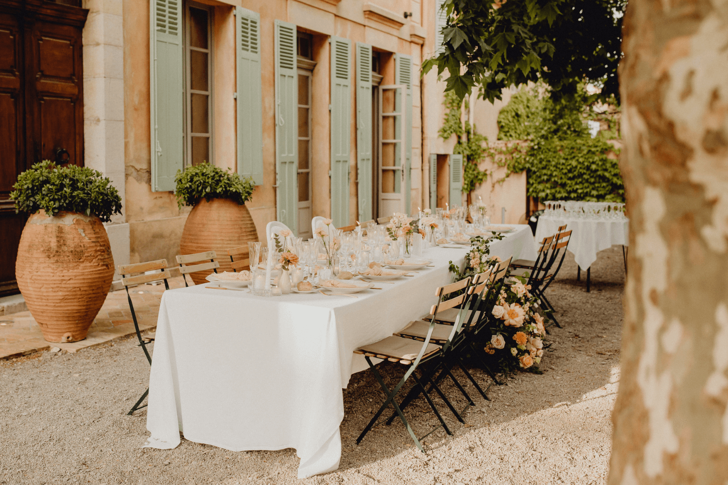 Une table de mariage en extérieur décorée d’une nappe blanche et de bouquets de roses.