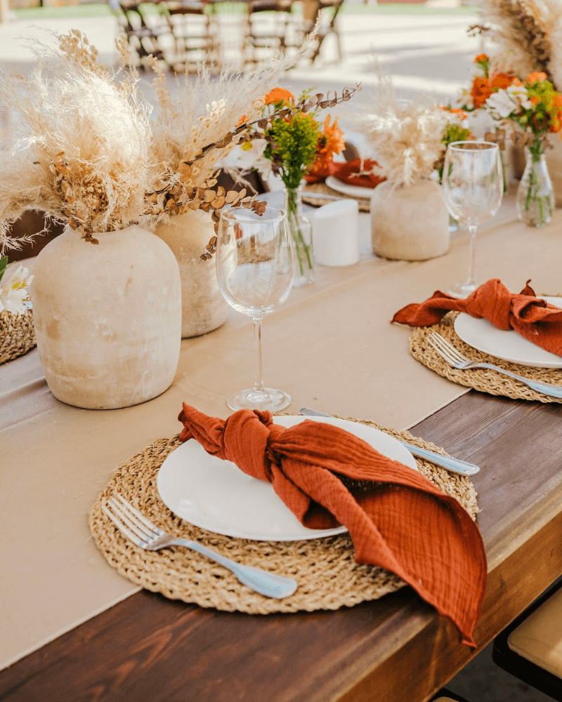 table de mariage en bois avec sous-plats en osier et assiettes décorées de serviettes couleur terracotta