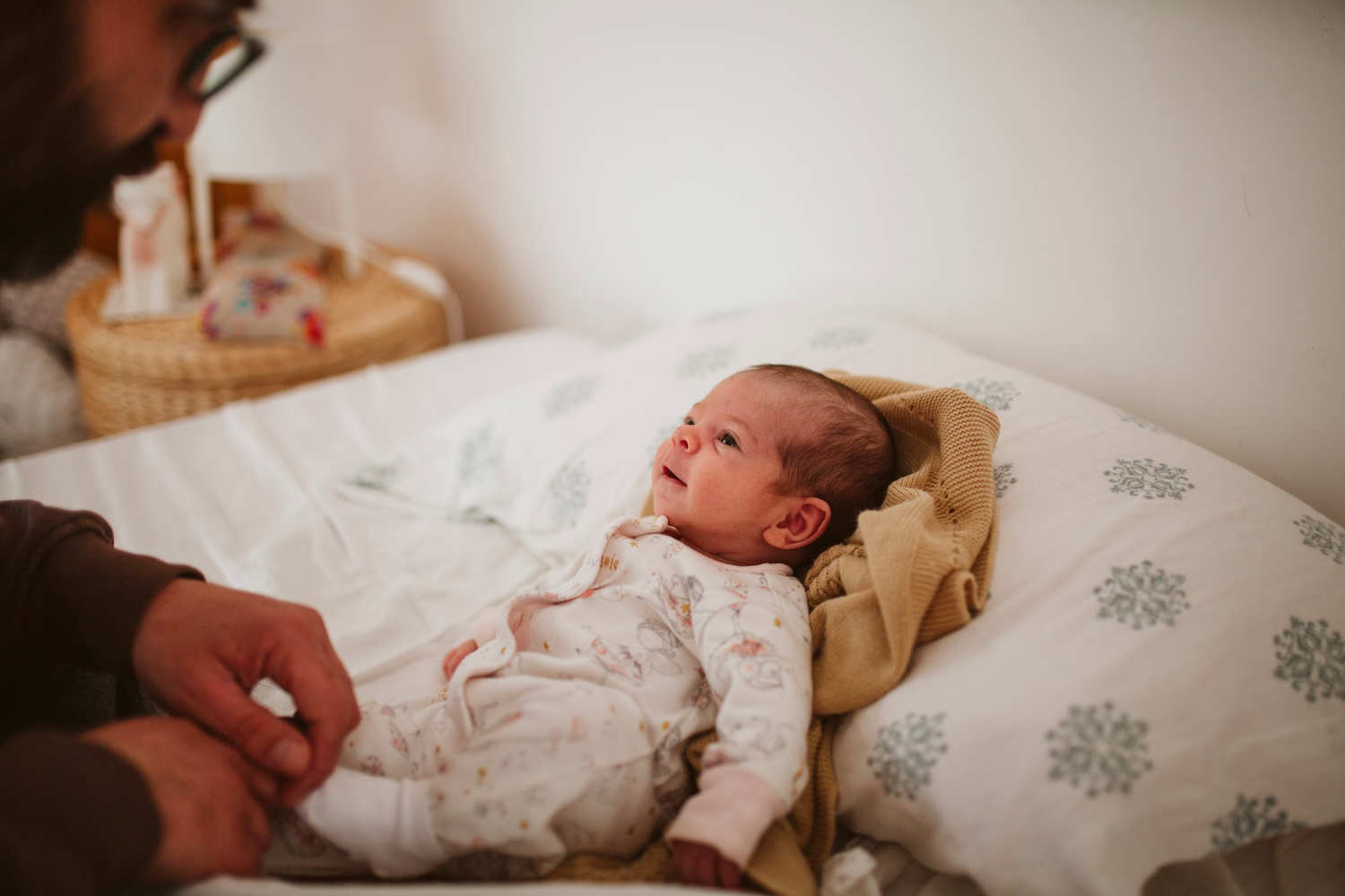 un bébé souriant allongé sur un lit, regardant son père.