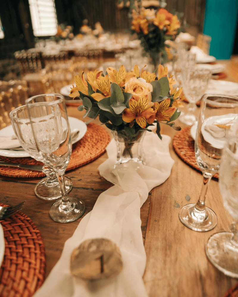 Une table de mariage en bois décorée avec des bouquets de fleurs aux couleurs orangées.